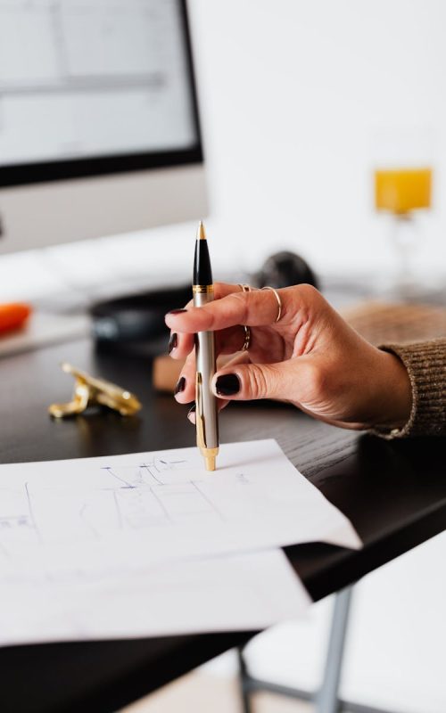 A woman's hand holding a pen, working on paperwork in a modern office setting.